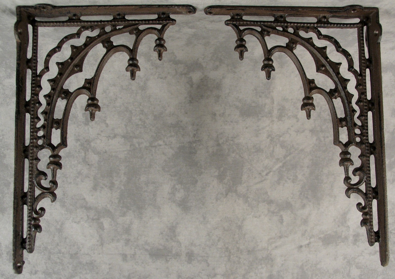 Pair of ornate dark metal arched brackets with scroll and finial details laid flat on a mottled gray surface